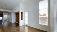 Located at 10400 East 29th Drive in the vibrant Stapleton community of Denver, Colorado, this single-floor home offers a thoughtfully designed interior that balances modern aesthetics with everyday functionality. The main living area immediately impresses with its soaring vaulted ceilings, which lend a sense of openness and airiness throughout the space. Rich, dark hardwood floors ground the interior and provide a warm contrast to the crisp white walls. Natural light flows generously through large windows fitted with adjustable blinds, creating a bright and welcoming atmosphere at any time of day. A glass-paneled exterior door further enhances the connection to the outdoors while allowing additional light to pour in. An accent wall in a deep earthy tone adds a layer of visual interest and architectural character, defining the transition between the living area and the adjoining spaces. Recessed ceiling vents indicate a modern HVAC system integrated seamlessly into the design. The overall ambiance is clean, contemporary, and inviting, with an open floor plan that promotes effortless flow between areas. This home reflects the well-planned, community-focused character that the Stapleton neighborhood of Denver is known for.