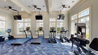 Located at 3001 Northeast Expressway in Atlanta, GA, this fitness center offers a thoughtfully designed exercise space that balances functionality with refined aesthetics. The room is distinguished by its elegant coffered ceilings adorned with crown molding and ceiling fans, lending a sense of openness and airiness uncommon in typical gym environments. Large, multi-pane windows line the walls on multiple sides, flooding the space with natural light and offering views of the surrounding greenery and outdoor amenities.

The exercise room is comprehensively equipped to support a full range of workout routines. Cardio equipment includes multiple treadmills and elliptical machines, each paired with wall-mounted flat-screen TVs for entertainment during workouts. The strength training area features a multi-station cable machine, a dedicated weight bench, a full dumbbell rack, medicine balls, stability balls, and battle ropes, providing ample options for resistance and functional training.

Patterned blue-toned carpeting covers the floor throughout, adding a polished, coordinated look to the space. Full-length mirrors along one wall enhance the sense of depth. The room is accessible via elegant French doors, and recessed lighting complements the natural light. The overall ambiance is bright, clean, and inviting, making it a well-appointed facility for fitness enthusiasts.