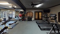 Located at 2600 Cole Ave in Dallas, Texas, this fitness center offers a comprehensive workout environment designed to support a wide range of exercise needs. The space is laid out across a single floor and is organized into distinct functional zones, allowing for seamless transitions between cardio, strength, and functional training.

The cardio area features a row of Cybex treadmills and elliptical machines, providing ample options for aerobic exercise. Adjacent to this zone, the strength training section is equipped with a multi-station Hoist cable machine system, a flat adjustable bench, and a dedicated free weights area complete with a full rack of dumbbells, kettlebells, and medicine balls in various weights. Stability balls of multiple sizes round out the functional training offerings.

Large wall-mounted mirrors throughout the space enhance the sense of openness and allow for proper form monitoring during workouts. Ceiling fans provide air circulation and comfort during intense sessions, complemented by overhead fluorescent lighting. The flooring consists of durable rubber or foam tile, ideal for high-traffic gym use.

The room features warm-toned accent walls with arched window details and dark wood trim, lending a refined aesthetic to the functional environment. A water fountain and resistance band station are also available along the perimeter walls. The space is accessible via double doors and includes an additional entry point, ensuring convenient access throughout.