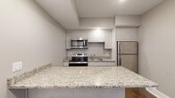 Located at 233 Pleasant St in Watertown, MA, this single-floor unit offers a thoughtfully designed layout with modern finishes throughout. The kitchen serves as a central highlight, featuring light granite countertops with subtle veining, light gray shaker-style cabinetry, and a full suite of stainless steel appliances, including an electric range, over-the-range microwave, and refrigerator. A generous kitchen island with a matching granite surface provides additional workspace and casual seating. Wood-look flooring runs throughout the main living areas, adding warmth to the otherwise neutral, contemporary palette of soft gray walls and white trim.

The living areas benefit from multiple windows fitted with horizontal blinds, allowing natural light to filter in and illuminate the hardwood floors. The bedrooms are well-proportioned, each featuring the same warm wood flooring, neutral wall tones, and windows that bring in natural light. The bathroom is finished with tile flooring, a granite-topped vanity, and a full tub-shower combination, maintaining the consistent modern aesthetic seen throughout the unit. Recessed lighting adds a polished touch to the overall clean and cohesive design of the space.