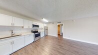 Located at 5903 Northwest 57th Court in Tamarac, Florida, this one-bedroom, one-bathroom unit offers a well-organized single-floor layout designed for comfortable everyday living. The open-concept kitchen and living area form the heart of the home, unified by warm wood-look flooring that extends throughout. The kitchen is fully equipped with stainless steel appliances—including a range, over-the-range microwave, dishwasher, and refrigerator—complemented by crisp white shaker cabinetry, a mosaic tile backsplash, and light countertops that create a clean, modern aesthetic. The living room is bright and airy, highlighted by a sliding glass door that opens to a private balcony, inviting natural light and outdoor views into the space. The generously sized bedroom features its own walk-in closet with built-in wire shelving, offering practical storage solutions. The bathroom is neatly appointed with a white vanity, a large mirror, and a full tub-shower combination. Textured ceilings and neutral wall tones carry throughout the unit, lending a cohesive and understated feel. A dedicated closet with louvered doors provides additional storage near the main living area.