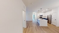 Located at 2568 E Glenn Ave in Auburn, Alabama, this single-floor home showcases a clean, modern design with an open and airy layout. Light oak-toned hardwood flooring flows through the main living and kitchen areas, creating a warm and cohesive feel throughout the space.

The kitchen is a standout feature, highlighted by a two-tone cabinetry scheme pairing crisp white upper cabinets with slate-blue lower cabinets, all accented with gold hardware. A large central island topped with white quartz countertops includes an undermount sink with a matte black faucet. Stainless steel appliances, recessed lighting, and stylish pendant lights complete the well-appointed kitchen.

The bedrooms are carpeted for comfort and each feature ceiling fans with light fixtures. Natural light enters through windows fitted with white blinds, giving the rooms a bright and inviting atmosphere. One bedroom provides access to a connected room, adding functional versatility.

The bathrooms are finished with white shaker-style vanity cabinetry, quartz countertops, undermount sinks, matte black fixtures, and large framed mirrors. One bathroom includes a tiled tub-shower combination with classic subway tile, while another features a more streamlined vanity layout. The consistent use of matte black accents throughout ties the home's design together cohesively.
