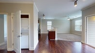 Located at 4003 Retreat Hill Way in Asheville, NC, this single-floor residence offers a thoughtfully designed open-concept layout that seamlessly connects the kitchen, dining, and living areas. Rich, dark hardwood flooring runs throughout the main living and kitchen spaces, providing a warm contrast to the neutral, light-toned walls and crisp crown molding that frame each room.

The kitchen is well-appointed with rich dark espresso cabinetry, granite countertops, and a full suite of black appliances including a refrigerator, range, and over-the-range microwave. A peninsula with additional counter space serves as a natural divider between the kitchen and the adjoining living area. Track lighting overhead provides focused illumination, while a tile backsplash adds a refined finishing touch.

The living area transitions to plush carpeting, creating a comfortable and distinct zone within the open floor plan. A ceiling fan with light fixture ensures year-round comfort, and multiple windows fitted with blinds allow for ample natural light and views of the surrounding greenery.

A dedicated laundry area features a stacked washer and dryer unit, adding convenient in-unit functionality. The bathroom is clean and functional, complete with a full soaking tub and shower combination with built-in shelving. Crown molding throughout the space adds an elegant, cohesive architectural detail.