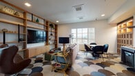 Located at 591 Pearl St in Eugene, Oregon, this thoughtfully designed single-floor space combines contemporary aesthetics with functional living. The interior is immediately distinguished by its bold, scallop-patterned carpet in tones of blue, brown, and cream, which flows seamlessly throughout the open-concept layout and serves as a striking design centerpiece.

The main living area is generously proportioned, anchored by a large sectional sofa and a floor-to-ceiling built-in wood shelving unit with integrated black metal accents, housing a mounted flat-screen television. A curated mix of seating — including a classic leather egg chair and a bar cart with gold detailing — adds character and versatility to the space. Large windows flood the room with natural light and frame views of the surrounding Eugene cityscape and distant mountains.

The kitchen is sleek and fully equipped, featuring stainless steel appliances including a range with a bold overhead hood, a built-in microwave, and a full-size refrigerator. Dark wood cabinetry pairs with a textured white tile backsplash, creating a refined, modern aesthetic.

A dining area with contemporary chairs sits adjacent to the living space, and a glass door opens directly onto a private outdoor terrace, offering additional seating and expansive open-air views — an exceptional amenity that extends the usable space of the interior.