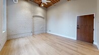 Located at 425 W Lakeside Ave in Cleveland's Lakeside neighborhood, this one-bedroom, one-bathroom unit showcases a striking combination of historic industrial architecture and contemporary upgrades. The living area features soaring ceilings with exposed wooden beam and plank construction, painted white brick walls, and light hardwood flooring throughout, creating a bright, loft-inspired atmosphere. Large black-framed windows invite abundant natural light and offer views of the surrounding urban streetscape. A ceiling fan adds both function and style to the open living space, which also features a decorative arched brick alcove as a standout architectural detail.

The kitchen is well-appointed with dark wood cabinetry, granite countertops, a subway tile backsplash, a black matte faucet, and a full suite of stainless steel appliances including a refrigerator, range, and over-the-range microwave. The bedroom is an intimate, quiet space with the same warm hardwood floors, an exposed brick column, and direct access to adjacent rooms. The bathroom features a single-vanity with wood cabinetry, a tub/shower combo, and clean white finishes. A dedicated closet completes this efficiently organized unit.