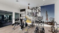 This fitness center in West Columbia, SC is a thoughtfully designed facility spanning a generous single floor. The space is divided into two distinct areas, each serving a specific purpose for members' workout needs.

The main exercise area features light wood-look flooring, white walls, and large windows that invite natural light and offer views of the outdoors. Ceiling fans maintain airflow throughout the space. This area is well-stocked with cardio equipment, including treadmills, ellipticals, recumbent bikes, upright bikes, a stair climber, and a rowing machine — all from TRUE Fitness. A dedicated strength training zone houses a comprehensive selection of weight machines and free weights. Bold, large-scale motivational murals depicting athletic imagery and a neon-style "Come Run With Us" graphic add an energizing visual character to the space.

A secondary room, accessible via a glass-paneled door, serves as a flexible studio for yoga, stretching, or light training. This calmer area features the same light wood flooring, a floor-to-ceiling mirror wall, wall-mounted television, mounted exercise mats, and a console with small dumbbells and plants, creating a clean and focused environment. Exposed wood beam accents add a warm architectural touch. Together, the two areas provide a comprehensive and inviting fitness experience.