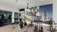 This fitness center in West Columbia, SC is a thoughtfully designed facility spanning a generous single floor. The space is divided into two distinct areas, each serving a specific purpose for members' workout needs.

The main exercise area features light wood-look flooring, white walls, and large windows that invite natural light and offer views of the outdoors. Ceiling fans maintain airflow throughout the space. This area is well-stocked with cardio equipment, including treadmills, ellipticals, recumbent bikes, upright bikes, a stair climber, and a rowing machine — all from TRUE Fitness. A dedicated strength training zone houses a comprehensive selection of weight machines and free weights. Bold, large-scale motivational murals depicting athletic imagery and a neon-style "Come Run With Us" graphic add an energizing visual character to the space.

A secondary room, accessible via a glass-paneled door, serves as a flexible studio for yoga, stretching, or light training. This calmer area features the same light wood flooring, a floor-to-ceiling mirror wall, wall-mounted television, mounted exercise mats, and a console with small dumbbells and plants, creating a clean and focused environment. Exposed wood beam accents add a warm architectural touch. Together, the two areas provide a comprehensive and inviting fitness experience.