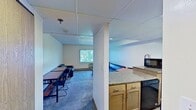 This 500-square-foot, single-floor apartment at 646 East College Avenue, Unit 3-119, in State College, PA, offers a compact and functional layout across five distinct areas. The bedroom accommodates two lofted wooden bed frames with built-in storage, illuminated by recessed panel lighting and featuring vertical blinds over a window with an in-wall HVAC unit for climate control. The full bathroom includes a tub/shower combo with chrome fixtures, a vanity mirror, and a toilet. The galley-style kitchen is equipped with granite-patterned countertops, light wood cabinetry, a black electric range with overhead ventilation, a dishwasher, a microwave, a sink, and durable hardwood-style flooring. The living area offers carpeted flooring, a textured ceiling, a large window with vertical blinds allowing natural light, baseboard heating, and an in-wall AC unit. A secondary living space provides additional seating and a desk area, also carpeted, making it suitable for studying or relaxing. The overall design is practical and utilitarian, well-suited for student housing near Penn State University.