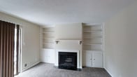 This two-story residence at Shelby Crossing offers a well-designed layout that balances comfort and practicality. The living area serves as a central gathering space, highlighted by a striking fireplace with a dark marble surround and matching hearth that anchors the room. Flanking the fireplace are symmetrical built-in shelving units, each featuring open display shelves above and closed cabinet storage below — a thoughtful design element that adds both character and functionality. The neutral, cream-toned walls complement the plush carpeting underfoot, creating a warm and inviting atmosphere throughout. A textured ceiling adds subtle dimension to the space. The clean, understated palette allows for versatile interior styling. Spread across two floors, the home provides a natural separation between living and private spaces, making it well-suited for a variety of lifestyles. The overall ambiance is quiet and comfortable, with classic architectural details that give the home a timeless, welcoming feel.