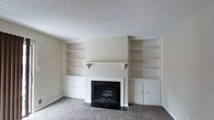 This two-story residence at Shelby Crossing offers a well-designed layout that balances comfort and practicality. The living area serves as a central gathering space, highlighted by a striking fireplace with a dark marble surround and matching hearth that anchors the room. Flanking the fireplace are symmetrical built-in shelving units, each featuring open display shelves above and closed cabinet storage below — a thoughtful design element that adds both character and functionality. The neutral, cream-toned walls complement the plush carpeting underfoot, creating a warm and inviting atmosphere throughout. A textured ceiling adds subtle dimension to the space. The clean, understated palette allows for versatile interior styling. Spread across two floors, the home provides a natural separation between living and private spaces, making it well-suited for a variety of lifestyles. The overall ambiance is quiet and comfortable, with classic architectural details that give the home a timeless, welcoming feel.