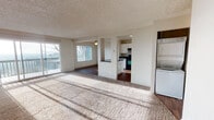 Located at 2101 SW Sunset Blvd in Renton, Washington, this single-floor residence offers a thoughtfully laid-out living space with a blend of comfort and functionality. The open-concept living and dining area is generously sized, featuring plush carpet flooring, a ceiling fan, and large sliding glass doors that lead to a private balcony overlooking the surrounding greenery. Natural light flows freely through multiple windows, creating a bright and welcoming atmosphere throughout.

The kitchen is well-appointed with white cabinetry, dark countertops, a black appliance suite including a range and refrigerator, and wood-look flooring. A pass-through counter connects the kitchen to the main living area, enhancing the open feel of the layout. A stacked washer and dryer unit is conveniently located within the residence, adding practical in-unit laundry access.

The bedrooms are carpeted and offer comfortable proportions, each with windows fitted with blinds for privacy and light control. The bathroom features a full soaking tub with a dark tile surround and wood-look flooring, providing a clean and functional space. Textured ceilings are consistent throughout the unit, contributing to its classic residential character.