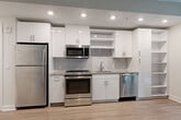 Located at 1111 New Jersey Ave SE in Washington, DC, Unit 207 is a thoughtfully designed modern residence that makes efficient use of its compact footprint. The open-plan layout seamlessly connects the living, dining, and kitchen areas, creating a bright and cohesive space anchored by light-toned hardwood flooring throughout. Large floor-to-ceiling windows with sleek black frames allow abundant natural light to pour in and offer views of the surrounding greenery, enhancing the airy feel of the interior.

The kitchen is outfitted with a full suite of stainless steel appliances, including a refrigerator, gas range, microwave, and dishwasher. Crisp white cabinetry with modern hardware extends to the ceiling, complemented by a subtle tile backsplash, granite countertops, and open shelving that adds both functionality and visual interest.

The bathroom features a soaking tub with an overhead shower, white subway tile surround with a decorative mosaic accent border, gray tile flooring, and granite-topped vanity. Two closets provide generous storage, one of which is a walk-in fitted with wire shelving. A dedicated laundry area and a hallway complete the layout. Recessed lighting throughout ensures a clean, contemporary ambiance across every room.