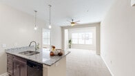 Located at 3340 Shipley St in North Charleston, SC, this single-floor, 3-bedroom, 2-bathroom home offers a well-designed open-concept layout with a clean, neutral aesthetic throughout. The kitchen serves as a central hub of the living area, showcasing dark wood cabinetry, granite countertops, black appliances, and a peninsula with bar seating illuminated by stylish pendant lighting. The kitchen flows seamlessly into the living area, which features plush carpeting, a ceiling fan, and large windows that fill the space with natural light. Hard surface flooring in the kitchen transitions smoothly into the carpeted living and bedroom areas. The primary bedroom is a comfortable retreat with two windows, a ceiling fan, and direct access to a spacious walk-in closet equipped with extensive wire shelving. Two additional bedrooms offer carpeted floors and neutral walls, ideal for versatile use. Both bathrooms are finished with granite-topped dark wood vanities and tiled tub-shower combinations. A dedicated laundry space houses a full-size washer and dryer. A hallway connects the bedrooms and provides additional organizational flow throughout the home, making this a functional and well-appointed residence.