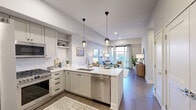 This thoughtfully designed 1-bedroom, 1-bathroom residence offers a seamless open-concept layout that maximizes every square foot of its single-floor plan. Warm hardwood flooring flows throughout the main living areas, connecting the kitchen, hallway, and living room in a cohesive, contemporary aesthetic.

The kitchen is a standout feature, showcasing soft gray shaker cabinetry, gleaming quartz countertops, and a full suite of stainless steel appliances including a French door refrigerator, gas range, built-in microwave, and dishwasher. A central island with an undermount sink and pendant lighting above provides both prep space and casual seating, making it ideal for cooking and entertaining.

The open living room is bright and airy, filled with natural light from large windows that offer outdoor views. A welcoming hallway entry connects the public and private areas of the home.

The bedroom is a serene retreat, featuring a textured blue accent wall, plush carpeting, and a large window that invites natural light. A dedicated closet provides ample storage. The bathroom is finished with marble-style tile, a dual-sink vanity with white cabinetry, and an elegantly tiled walk-in shower, delivering a clean, spa-like aesthetic throughout.
