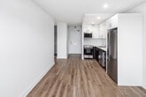 Located at 600 John St in Hamilton, Ontario, unit 108 is a single-floor residence designed with a clean, modern aesthetic throughout. Light wood laminate flooring runs consistently across all rooms, creating a cohesive and warm feel that complements the crisp white walls and trim.

The open living area benefits from a large window that frames views of surrounding greenery, allowing natural light to fill the space. Baseboard heating units are positioned beneath the windows, ensuring year-round comfort. The textured white ceiling adds subtle character to the otherwise streamlined interior.

The kitchen is well-equipped with a contemporary two-tone design, featuring high-gloss white upper cabinetry paired with dark wood-finish lower cabinets and white countertops. Stainless steel appliances include a refrigerator, electric stove, built-in dishwasher, and a microwave, all set against a clean white backsplash with recessed lighting above.

The bedroom offers a generous layout with a full-width sliding door closet providing ample storage, along with an adjacent secondary storage area with open shelving. Additional rooms are bright and open, with windows fitted with roller blinds offering privacy and light control. The overall ambiance is clean, functional, and move-in ready.