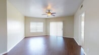 This single-floor residence offers a practical and comfortable layout with a cohesive, neutral design throughout. The spacious living area serves as the heart of the home, featuring rich hardwood-style flooring, a ceiling fan with light fixture, and abundant natural light streaming through a large window and a sliding glass door fitted with vertical blinds. The open layout connects seamlessly to the kitchen, which is equipped with white cabinetry, a breakfast bar peninsula, granite-style countertops, a double sink, and white appliances including a range, microwave, and dishwasher — all set atop matching hardwood-style flooring. Bedrooms are carpeted for comfort and include ceiling fans, windows with blinds, and access to natural light; one bedroom features a sliding glass door and another includes a spacious built-in closet with bi-fold doors. The primary bedroom connects directly to a full bathroom with a wide vanity, granite-style countertop, a large mirror, and hardwood-style flooring. A second bathroom provides a tub-shower combination with tiled surround, a single-sink vanity, and matching finishes. Warm beige tones and white trim are consistent throughout, creating a clean, inviting ambiance.