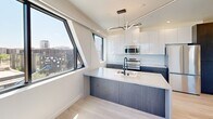 Located in Phoenix, AZ, this thoughtfully designed 2-bedroom, 1-bathroom unit delivers a clean, modern aesthetic throughout. Light wood-toned flooring runs continuously across the space, complementing the bright white walls and creating an open, airy atmosphere. The kitchen is a standout feature, boasting high-gloss white upper cabinetry, contrasting dark lower cabinets, a large waterfall-edge island with an integrated sink, stainless steel appliances, and a sculptural pendant light fixture. Architecturally distinctive angled windows flood the kitchen and living areas with natural light while framing panoramic views of the surrounding Phoenix cityscape. Both bedrooms are well-proportioned, each equipped with ceiling fans and large black-framed windows that invite abundant sunlight and offer elevated city views. The primary bedroom provides a comfortable, serene retreat. The bathroom features a clean, minimalist design with a walk-in shower accented by matte black fixtures and hardware, white cabinetry with a gray countertop, and light wood flooring that ties the space cohesively together. The unit's modern architecture and carefully selected finishes make it a compelling urban residence in the heart of Phoenix.