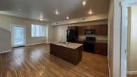 This 960-square-foot, two-story residence offers 2 bedrooms and 2 bathrooms across two well-defined floors. The ground floor (500 sq ft) features an open-concept kitchen and living area with warm hardwood-style flooring throughout. The kitchen is equipped with dark wood cabinetry, granite-style countertops, a central island with a sink, black appliances including a gas range and refrigerator, and recessed lighting. The living area flows naturally from the kitchen and includes a front entry door with an adjacent staircase. A half bathroom with a pedestal sink and hardwood-style flooring is also located on this floor. The upper floor (460 sq ft) houses both bedrooms, a full bathroom, and a closet. The primary bedroom (150 sq ft) features plush carpet flooring and a sliding glass door leading to a private outdoor balcony. The second bedroom is similarly carpeted and receives natural light through a window. The full bathroom includes a dark wood vanity with a countertop sink, a tub/shower combination, and a window for natural light. Neutral beige tones are consistent throughout both floors, creating a cohesive and functional living environment.