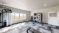 Located at 522 Sweetgrass Dr in Brookings, South Dakota, this dedicated exercise room offers a thoughtfully designed fitness space suited for a comprehensive workout. The room is finished with stylish herringbone-patterned carpet tiles in varying shades of gray, lending a modern, clean aesthetic throughout.

Large windows line one wall, flooding the space with natural light and framing open views of the surrounding South Dakota landscape — an energizing backdrop for any workout session. The room is equipped with an impressive array of fitness equipment, including a multi-station cable machine, a dumbbell rack with a full range of hex weights, a stability ball rack holding multiple exercise balls, and a TAG-branded medicine ball rack stocked with colorful weighted balls in various sizes. An adjustable workout bench adds further versatility for strength training.

A distinctive decorative accent wall featuring a bold geometric circle pattern adds visual interest and anchors one end of the room, where a wall-mounted water fountain provides convenient hydration. Recessed lighting complements the natural light, ensuring the space remains bright at any time of day. Clean white walls and dark baseboards complete the polished, contemporary design, making this fitness room both functional and visually appealing.