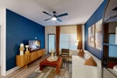 Located in Spring, TX, this well-appointed 2-bedroom, 2-bathroom residence offers a thoughtfully designed single-floor layout. The open-concept living and kitchen area serves as the heart of the home, where a striking deep-blue accent wall anchors the living room, complemented by light wood-look flooring, a ceiling fan, and large windows dressed in warm rust-toned curtains that invite natural light. The kitchen is outfitted with white shaker-style cabinetry, a white quartz peninsula with bar seating, stainless steel appliances including a side-by-side refrigerator and dishwasher, and sleek pendant lighting overhead. The primary bedroom features a comfortable layout with ample closet space, while the second bedroom makes a bold statement with a dramatic black-and-white diamond-patterned accent wall and a ceiling fan. Two well-designed bathrooms serve the home: one with a glass-enclosed walk-in shower featuring large-format white tile, and the other with a soaking tub and tiled surround. A hallway connects the spaces efficiently, with additional closets providing generous storage. The overall aesthetic is modern and cohesive, blending bold design choices with clean, neutral finishes throughout.