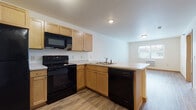 This single-floor unit is designed with a practical, open layout that promotes a comfortable and functional living experience. The kitchen serves as a central feature, equipped with light maple cabinetry offering generous storage, a full suite of black appliances including a refrigerator, electric range, over-the-range microwave, and dishwasher, and a peninsula with a built-in sink that provides additional counter space. The peninsula opens directly to the living area, creating a seamless open-concept flow ideal for everyday living.

Wood-look flooring runs consistently throughout the unit, lending a cohesive and clean aesthetic to each room. The bedrooms are well-proportioned, each featuring windows that bring in natural light and offer views of the surrounding neighborhood. A wall-mounted air conditioning unit is installed in one of the bedrooms, providing dedicated climate control.

The bathroom includes a light wood vanity with a white countertop, a toilet, and a bathtub/shower combination. A dedicated laundry area houses a stacked washer and dryer unit, adding significant convenience. Throughout the space, neutral wall tones and warm wood trim complement the overall understated and move-in-ready aesthetic.