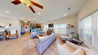 Located at 866 Logan St in Rogersville, Missouri, this single-floor community space offers a thoughtfully designed open-plan layout that seamlessly connects multiple functional zones. Light-toned hardwood-style flooring runs throughout, enhancing the sense of openness and continuity across the entire space.

The living area is generously sized, furnished with comfortable gray sofas, accent chairs, and a coffee table arranged around a wall-mounted flat-screen TV. Large windows line the walls, flooding the room with natural light and offering pleasant views of the surrounding landscape. Ceiling fans with recessed lighting ensure year-round comfort.

Adjacent to the living area is a dedicated dining zone featuring a spacious rectangular table with upholstered chairs, ideal for group gatherings. A fitness area with a treadmill and exercise equipment is also integrated into the layout, providing residents with convenient access to wellness amenities.

The kitchen is well-appointed with rich dark wood cabinetry, granite-style countertops, full-size appliances including a refrigerator and microwave, and a large peninsula bar with vibrant teal metal barstools — a lively focal point of the space. Warm, rustic décor accents, including lodge-themed signage, give the interior a welcoming, casual character. An exterior door provides access to an outdoor area with a pool, extending the usable space beyond the interior.