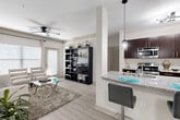 This single-floor residence offers a thoughtfully designed open-concept layout that seamlessly connects the main living areas. The living room is bright and welcoming, featuring light hardwood-style flooring, a ceiling fan, and large windows that allow ample natural light to fill the space. A bold teal abstract artwork anchors one wall, adding a vibrant touch to the neutral palette.

The kitchen is a functional highlight, outfitted with dark espresso cabinetry, a classic white subway tile backsplash, stainless steel appliances — including a refrigerator, range, microwave, and dishwasher — and granite countertops throughout. A peninsula with bar seating and pendant lighting serves as both a dining and casual gathering spot.

Two bedrooms provide comfortable retreats, each carpeted and finished with neutral tones. The rooms offer generous space and well-proportioned layouts suitable for full bedroom furniture sets. Two bathrooms mirror the kitchen's design sensibility, featuring dark cabinetry with sleek hardware, granite countertops, large vanity mirrors, and shower-tub combinations with tiled surrounds. The overall aesthetic throughout the residence is clean, contemporary, and cohesive, with a consistent use of neutral tones accented by modern fixtures and finishes.