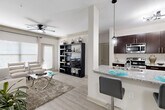 This single-floor residence offers a thoughtfully designed open-concept layout that seamlessly connects the main living areas. The living room is bright and welcoming, featuring light hardwood-style flooring, a ceiling fan, and large windows that allow ample natural light to fill the space. A bold teal abstract artwork anchors one wall, adding a vibrant touch to the neutral palette.

The kitchen is a functional highlight, outfitted with dark espresso cabinetry, a classic white subway tile backsplash, stainless steel appliances — including a refrigerator, range, microwave, and dishwasher — and granite countertops throughout. A peninsula with bar seating and pendant lighting serves as both a dining and casual gathering spot.

Two bedrooms provide comfortable retreats, each carpeted and finished with neutral tones. The rooms offer generous space and well-proportioned layouts suitable for full bedroom furniture sets. Two bathrooms mirror the kitchen's design sensibility, featuring dark cabinetry with sleek hardware, granite countertops, large vanity mirrors, and shower-tub combinations with tiled surrounds. The overall aesthetic throughout the residence is clean, contemporary, and cohesive, with a consistent use of neutral tones accented by modern fixtures and finishes.