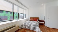 Located at 253 Academy St in Jersey City, NJ, this single-floor studio offers a clean, modern design with a well-planned open layout that efficiently combines living, sleeping, and dining functions. Warm hardwood flooring runs throughout, providing a cohesive look across every area of the space.

The sleeping area is positioned along a wall of large windows fitted with roller shades, allowing natural light to filter in while offering views of the surrounding Jersey City skyline. Recessed ceiling lighting complements the natural brightness, keeping the space well-lit at all hours.

The kitchenette features crisp white cabinetry, white appliances including a refrigerator, microwave, and range, and ample counter space. Adjacent to the kitchen is a compact dining area with a round white table and matching chairs — a functional yet stylish spot for everyday meals.

The bathroom is finished with clean white walls, wood-look flooring, a white vanity with storage, and a mirrored medicine cabinet, creating a tidy and practical space. A wall-mounted towel bar adds a finishing touch.

The unit's entry area is minimal and welcoming, with a solid door and white walls that maintain the space's bright, uncluttered aesthetic. Overall, this studio presents a well-organized, light-filled urban living space ideally situated in the heart of Jersey City.