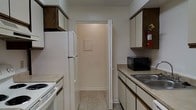 Located at 10875 Abercorn St in Savannah, Georgia, this single-floor residence offers a practical and well-organized layout designed for comfortable everyday living. The kitchen is arranged in a classic galley configuration, maximizing efficiency with countertops and storage running along both sides. White cabinetry with dark wood trim accents provides generous storage space, while light-toned laminate countertops offer ample workspace. The kitchen is equipped with essential appliances, including a white refrigerator, a range, and a countertop microwave, alongside a double-basin sink. Light tile flooring runs throughout the kitchen, contributing to a clean and easy-to-maintain environment. A doorway at the end of the kitchen connects to an adjacent area, suggesting a functional flow between spaces throughout the home. The neutral white walls and light-toned finishes create a bright and airy atmosphere, giving the space an open and inviting feel. Overall, this single-floor home in Savannah presents a straightforward, practical design well-suited for those seeking a comfortable and efficiently organized living environment in a convenient Savannah location.