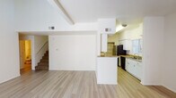 This two-story residence offers a thoughtfully designed layout spread across two levels, combining functional living spaces with clean, neutral finishes throughout. The main level centers around a spacious, open-concept living and dining area characterized by dramatically high vaulted ceilings that create an airy, expansive atmosphere. A tile-surround fireplace anchors the living room, while large vertical-blind-dressed sliding glass doors invite abundant natural light. Light-toned hardwood-style flooring runs throughout the main living areas, adding warmth and cohesion to the space.

The galley-style kitchen is well-appointed with white shaker cabinetry, granite-look countertops, stainless steel appliances including a range, microwave, and refrigerator, along with a double basin sink. A peninsula counter connects the kitchen to the living area, enhancing the open flow. A dedicated pantry provides additional storage.

Upstairs, the carpeted bedrooms offer a quieter retreat, each featuring large windows with vertical blinds that bring in natural light and views of surrounding greenery. The bathrooms are finished with light wood-style flooring, vanity cabinetry, and well-lit mirrors. A practical laundry area with a full-size washer and dryer is conveniently located within the unit, complemented by built-in shelving for storage.