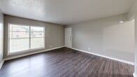 Located at 11117 Lochmond Cir in Dallas, TX, this single-story, 2-bedroom, 1-bathroom home offers a practical and cohesive layout across its single floor. Consistent dark hardwood-style flooring flows throughout every room, complemented by neutral gray walls and crisp white trim, creating a clean and unified aesthetic.

The living room is a welcoming open space featuring a textured ceiling, a front entry door, and a window that allows natural light to fill the room. Adjacent to the living area, the kitchen is efficiently designed with white cabinetry, light speckled countertops, a peninsula for additional prep or casual seating, and black appliances including a refrigerator and electric range. A double-basin sink sits beneath a window overlooking the exterior.

Both bedrooms are well-proportioned and bright, each featuring two windows that bring in generous natural light and offer views of the surrounding neighborhood. The primary bedroom provides a comfortable amount of space, while a hallway area with multiple doors offers access to closets and the shared bathroom.

The bathroom is neatly appointed with a tiled tub-shower combo, a window for ventilation, a speckled countertop vanity, and hardwood-style flooring consistent with the rest of the home. Overall, the space presents a tidy, move-in-ready feel with consistent finishes throughout.