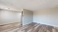 Located at 8201 Madison Ave in Indianapolis, IN, this 2-bedroom, 1-bathroom single-floor unit offers a practical and well-appointed layout. The living room is bright and open, finished with durable wood-look vinyl plank flooring in a warm gray tone and neutral gray walls. A large sliding glass door fills the space with natural light and provides outdoor access. The kitchen is a standout feature, equipped with dark gray shaker-style cabinetry extending to the ceiling for ample storage, white countertops, and a full suite of stainless steel appliances including a gas range, microwave, dishwasher, and refrigerator. Light wood-look flooring continues throughout the kitchen. Both bedrooms are carpeted in a neutral tan tone and feature windows with blinds that invite natural light. The primary bedroom includes two closets—one walk-in and one standard—offering generous storage. A hallway connects the private areas of the unit. The full bathroom is clean and functional, featuring a tiled shower/tub combo, a single vanity with mirror, and a window for natural light. Textured ceilings and clean white trim are consistent throughout, giving the space a cohesive, move-in-ready feel.