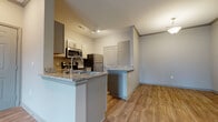 This single-story residence offers a well-designed layout with a cohesive mix of materials and finishes throughout. The kitchen serves as a central highlight, featuring gray shaker-style cabinetry, granite countertops, and a full suite of stainless steel appliances including a range, microwave, refrigerator, and dishwasher. A peninsula with a granite overhang provides additional workspace and opens toward the living area, enhancing the sense of connectivity within the space. Wood-look plank flooring flows through the kitchen, living, and entry areas, lending warmth and continuity.

The entry area is generously sized with crown molding details and wood-look flooring, while the living space benefits from multiple windows that invite natural light. Bedrooms are finished with plush carpet and feature access to walk-in closets with built-in shelving. Windows in the bedrooms provide outdoor views and additional natural light. The bathroom includes a granite-topped vanity with gray cabinetry that mirrors the kitchen's design language, maintaining a consistent aesthetic throughout the unit. Neutral wall tones complement the overall palette, creating a clean and move-in-ready environment.