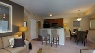 Located at 7331 Skyline Dr in Columbus, Ohio, this single-floor residence offers a thoughtfully designed open-concept layout that seamlessly connects the main living spaces. The living area is carpeted and warmly lit, creating a comfortable and inviting atmosphere, with ample room for seating and relaxation. Adjacent to the living space is a dedicated dining area, providing a natural flow for everyday living and entertaining. The kitchen is well-appointed with rich, warm-toned cabinetry, dark granite-style countertops, and black appliances, including a built-in microwave. A peninsula-style breakfast bar with seating for multiple bar-height chairs serves as both a functional workspace and a casual dining spot, acting as the central hub between the kitchen and living areas. The neutral, warm wall tones and plush carpeting carry throughout the space, contributing to a cohesive and welcoming ambiance. A hallway visible from the main area leads to additional rooms, suggesting a practical and efficient floor plan. The overall design balances comfort and functionality, making it a well-suited space for everyday living.