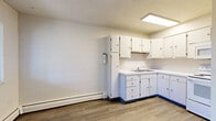 Located at 509 18th St in Greeley, Colorado, this 2-bedroom, 1-bathroom single-floor unit offers a practical and straightforward layout across a compact but efficient floor plan. The kitchen is well-equipped with ample white cabinetry, light wood-look flooring, a double basin sink, and white appliances including an electric range, over-the-range microwave, and refrigerator — all illuminated by overhead fluorescent lighting. The kitchen connects to a combined living and dining area, providing an open and functional common space. Both bedrooms feature plush carpeting, textured ceilings, natural light from windows, and individual closets for storage. The primary bedroom offers a comfortable footprint with room for standard furnishings. The full bathroom is finished with white subway tile wainscoting, mosaic tile flooring, a tub-shower combination, and clean, neutral tones throughout. A hallway connects the main living areas to the bedrooms and bathroom, with four closets distributed throughout the unit providing generous storage. Baseboard heating is present in multiple rooms. The overall aesthetic is clean and neutral, with white walls and block-style wall textures visible in several rooms.