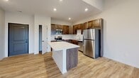 Located at 1220 W Highland Blvd in Lincoln, Nebraska, this one-bedroom, one-bathroom residence offers a thoughtfully designed single-floor layout that maximizes functionality and comfort. The open-concept living and kitchen area is anchored by a standout kitchen featuring rich, dark-stained wood cabinetry, a large center island with a light marble-style countertop, and a full suite of stainless steel appliances including a refrigerator, range, and microwave. Light wood-style flooring flows throughout the main living areas, enhancing the bright, clean aesthetic. Recessed lighting illuminates the space, while a sliding glass door in the living room opens to a private balcony overlooking open, scenic Nebraska landscape. The bedroom is a comfortable retreat finished with plush carpeting, a ceiling fan, and a window framing peaceful outdoor views. A dedicated closet provides added storage convenience. The bathroom is finished with wood-toned cabinetry, a marble-style countertop, and a full tub-shower combination. A hallway connects the rooms efficiently, completing this well-organized and modern living space.