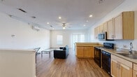 This two-bedroom, two-bathroom residence is thoughtfully arranged across two floors, offering a functional and comfortable layout. The main floor serves as the social hub of the home, featuring an open-concept living, dining, and kitchen area bathed in natural light from large windows and a sliding glass door fitted with vertical blinds. The kitchen is well-appointed with light maple cabinetry, stone-toned countertops, and stainless steel appliances including a refrigerator, microwave, and dishwasher, complemented by wood-look flooring that flows throughout the main level. A ceiling fan with overhead lighting anchors the living area, which also includes a wall-mounted mini-split HVAC unit for climate control. Recessed lighting adds a clean, modern touch throughout. The upper floor houses both bedrooms, each carpeted for comfort. The spacious primary bedroom features a ceiling fan, multiple windows, and a sliding door that fills the room with natural light. A hallway connects the bedrooms to two full bathrooms, one of which includes a full soaking tub with a shower combo and built-in shelving. Two closets and dedicated staircase access complete the upper level, making this a well-organized and practical residence.