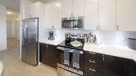 This single-floor residence presents a cohesive, contemporary design characterized by crisp white walls, neutral tones, and an airy ambiance throughout. The living room serves as a welcoming central space, featuring light hardwood-style flooring, a comfortable neutral sofa accented with gray and white pillows, and bold framed artwork as a focal point. A ceiling fan overhead and multiple windows with blinds allow natural light to fill the room.

The kitchen is outfitted with a striking two-tone cabinet scheme — dark lower cabinets contrasted by white upper cabinets — paired with white countertops, a classic subway tile backsplash, and a full suite of stainless steel appliances. Light wood-style flooring and a window above the sink contribute to its bright, functional character.

The bedrooms are carpeted and well-proportioned, each equipped with ceiling fans and large windows dressed with sheer curtains that invite generous natural light and outdoor views. The primary bedroom connects to a walk-in closet with wire shelving and a clean, bright en-suite bathroom featuring a glass-enclosed shower, large-format tile flooring, and modern brushed nickel fixtures throughout.
