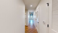 Located at 219 N Columbus St in Lancaster, Ohio, this one-bedroom, one-bathroom unit blends industrial character with modern finishes across a single floor. The open-concept living and kitchen area is the centerpiece of the space, showcasing rich hardwood floors, whitewashed exposed brick walls, and soaring ceilings with visible ductwork that lend an authentic loft aesthetic. Large multi-pane windows allow generous natural light to fill the space while offering views of the surrounding area. The kitchen is well-appointed with crisp white cabinetry, stainless steel appliances including a full-size refrigerator with ice maker, electric range, built-in microwave, and dishwasher, all complemented by clean countertops and a single-basin sink. The bedroom is a comfortable, carpeted retreat with neutral walls offering a quiet contrast to the open living area. It is served by a dedicated walk-in closet featuring wire shelving on multiple walls, providing substantial storage capacity. The bathroom is finished with a tasteful hexagonal tile floor, a vanity with undermount sink and taupe cabinetry, black hardware accents, and a sliding glass-door shower stall with subway tile surround. A hallway connects the private areas of the unit seamlessly, completing this well-designed and characterful residence.