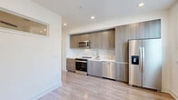 Located at 3050 Del Hombre in Walnut Creek, California, this efficiently designed single-floor unit offers a clean, contemporary aesthetic throughout. Light-toned wood-look flooring runs seamlessly across the living spaces, complementing the bright white walls and recessed lighting that keep the interior feeling open and airy.

The kitchen and dining area form the heart of the unit, showcasing modern flat-front cabinetry in a warm wood-grain finish, a neutral tile backsplash, and a full suite of stainless steel appliances including a side-by-side refrigerator with ice and water dispenser, a dishwasher, a range, and an over-the-range microwave. A large window allows natural light to fill the space, enhancing its contemporary feel.

Additional rooms feature generous windows fitted with horizontal blinds, providing ample natural light and outdoor views, while ceiling fans add comfort and functionality. One room benefits from a clerestory-style window, maintaining privacy while still bringing in natural light.

The bathroom is finished with large-format marble-look porcelain tile on both the floors and shower surround, paired with a floating wood-grain vanity and brushed gold fixtures throughout. A stacked washer and dryer unit is conveniently integrated into the bathroom, maximizing the efficient use of space. Overall, the unit presents a fresh, modern living environment with thoughtful finishes.