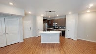 This well-designed single-floor residence offers a cohesive blend of modern finishes and functional living spaces. The open-concept kitchen serves as the heart of the home, showcasing dark espresso cabinetry that extends to the ceiling, light quartz countertops, and a sleek horizontal glass tile backsplash. A curved waterfall island with an undermount sink anchors the space, illuminated by a pair of striking geometric pendant lights. Stainless steel appliances, including a French door refrigerator, electric range, over-the-range microwave, and a built-in beverage cooler, complete the culinary suite. Rich wood-look plank flooring flows seamlessly from the kitchen through the open living and dining areas, where a ceiling fan and a set of glass patio doors invite natural light and outdoor access. The bedrooms are carpeted for comfort, each featuring windows with blinds. The bathrooms are finished with dark wood vanities, granite-topped double sinks, framed mirrors, and modern light fixtures. One bathroom features a tiled tub-shower combination with a rain showerhead, while the other offers accessible grab bars. Recessed lighting and a neutral color palette throughout create a clean, contemporary ambiance.