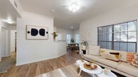 This single-floor, 3-bedroom, 1-bathroom home offers a thoughtfully designed layout that maximizes functionality and comfort. The bright living room features warm hardwood-style flooring, crown molding, a ceiling fan, and multiple windows dressed with horizontal blinds that filter in generous natural light. A pass-through connects the living area to the kitchen, creating an open, airy feel throughout the main living space.

The galley-style kitchen is outfitted with warm wood cabinetry, white countertops, and black appliances including a refrigerator, range, microwave, and dishwasher. It opens conveniently toward the dedicated laundry room, which houses a full-sized washer and dryer alongside built-in shelving.

The adjacent dining room is bright and inviting, with large windows offering views of lush greenery outside — an ideal setting for everyday meals or entertaining.

The primary bedroom features plush carpeting, a ceiling fan, and a walk-in closet. The additional bedrooms are comfortably sized, each with closet space. The shared bathroom includes a double-sink vanity with warm wood cabinetry, a large mirror, and Hollywood-style lighting.

Throughout the home, a neutral color palette and consistent flooring create a cohesive, modern aesthetic that is both welcoming and versatile.