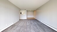 This 730-square-foot, single-floor apartment offers a practical and well-designed layout encompassing 2 bedrooms, 1 bathroom, a combined kitchen and living room, and a hallway. Neutral gray walls and clean white trim are consistent throughout, creating a cohesive, modern aesthetic. The living room is spacious and carpet-floored, featuring baseboard heating and large sliding glass doors that provide natural light and outdoor views of green surroundings. The kitchen is efficiently laid out with gray shaker-style cabinetry, marble-look countertops, white subway tile backsplash, light wood-look vinyl flooring, and black stainless appliances including a gas range, microwave, refrigerator, and dishwasher. A pass-through opening connects the kitchen to the living area. The primary bedroom measures 160 square feet and features plush carpet, a double-door closet, and a baseboard heater. The second bedroom is similarly finished with carpet, a window offering outdoor views, and baseboard heating. The shared bathroom is well-appointed with dual sinks set in a long vanity with gray cabinetry, a large mirror, white countertops, light wood-look flooring, and a separate tub/shower enclosure accessible through a private door.
