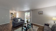 This single-floor residence offers a well-organized layout that balances comfort and functionality across its key living spaces. The living room serves as the heart of the home, featuring dark wood-style laminate flooring, neutral gray walls, and a textured ceiling. Multiple windows and a sliding glass door flood the space with natural light while providing direct access to an outdoor area. A ceiling fan adds an additional layer of comfort to the adjoining dining area, which accommodates a glass-top dining table and benefits from its own window overlooking the exterior.

The kitchen is efficiently designed with white cabinetry, black appliances including a range and dishwasher, and ample counter space. It connects seamlessly to the dining area, making the space practical for everyday use and entertaining.

The primary bedroom is a calm retreat, finished with plush carpet and neutral walls. It features a spacious closet with bifold doors and is large enough to accommodate a queen-sized bed with room to spare. A second bedroom, also carpeted, offers a cheerful and versatile space suitable for a child's room or guest room.

The bathroom is clean and functional, featuring wood-style flooring, a tub-shower combination, and a pedestal-style sink. Throughout the residence, the consistent use of neutral tones and hard-surface flooring in the main areas creates a cohesive and inviting atmosphere.