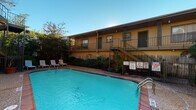This ground-floor unit is part of a well-established multi-unit residential complex characterized by classic brick exterior construction and a warm, neutral color palette. The building's façade showcases textured brick walls paired with wood-paneled siding, lending the property a durable and timeless architectural character. Units are accessed via covered concrete walkways, providing sheltered entry points highlighted by large windows with horizontal blinds that allow natural light to filter in.

The complex features shared outdoor amenities, most notably a generously sized swimming pool with clear blue water, surrounded by a brick-paved deck and furnished with lounge chairs — ideal for relaxation. The pool area is framed by mature trees and lush tropical plantings, offering a private, shaded retreat. An upper level is accessible via an open metal staircase, and decorative wrought iron gating adds a distinctive visual element at entry points throughout the property.

Safety infrastructure is well-integrated into the building's common areas, with fire hose cabinets mounted flush into the brick walls at accessible locations along the corridors. Landscaped greenery lines the exterior pathways, contributing to an inviting outdoor atmosphere. The overall ambiance of the property is practical and community-oriented, with shared spaces designed to complement comfortable residential living.