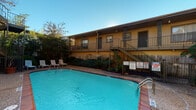 This ground-floor unit is part of a well-established multi-unit residential complex characterized by classic brick exterior construction and a warm, neutral color palette. The building's façade showcases textured brick walls paired with wood-paneled siding, lending the property a durable and timeless architectural character. Units are accessed via covered concrete walkways, providing sheltered entry points highlighted by large windows with horizontal blinds that allow natural light to filter in.

The complex features shared outdoor amenities, most notably a generously sized swimming pool with clear blue water, surrounded by a brick-paved deck and furnished with lounge chairs — ideal for relaxation. The pool area is framed by mature trees and lush tropical plantings, offering a private, shaded retreat. An upper level is accessible via an open metal staircase, and decorative wrought iron gating adds a distinctive visual element at entry points throughout the property.

Safety infrastructure is well-integrated into the building's common areas, with fire hose cabinets mounted flush into the brick walls at accessible locations along the corridors. Landscaped greenery lines the exterior pathways, contributing to an inviting outdoor atmosphere. The overall ambiance of the property is practical and community-oriented, with shared spaces designed to complement comfortable residential living.
