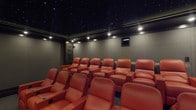 Located at 3401 W Olive Ave in Burbank, California, this dedicated private screening room delivers an immersive, cinema-quality experience from top to bottom. The room's most striking feature is its deep black fiber optic ceiling, studded with pinpoints of light that replicate a night sky, instantly setting a theatrical mood upon entry. Recessed and perimeter lighting supplements the ambiance, casting a warm, controlled glow across the entire space.

Seating is arranged in a tiered configuration across multiple rows, accommodating a generous number of guests in rich, burnt-orange leather recliners. Each seat is equipped with integrated cup holders and power reclining capability, mirroring the comfort of a high-end commercial cinema. The tiered layout ensures unobstructed sightlines from every position in the room.

The walls are finished in a muted, dark gray tone that minimizes light reflection and enhances the on-screen viewing experience. Decorative Art Deco-style lattice panels are symmetrically placed along the side walls, adding architectural elegance and visual depth. Textured carpeting in a complementary dark gray runs throughout the floor, contributing to the room's acoustic performance. A central console table with a built-in control surface is positioned mid-room, offering convenient access to system controls. The result is a polished, fully appointed screening environment purpose-built for film and entertainment.