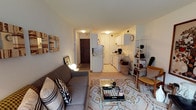 This single-floor residence offers a thoughtfully arranged layout that makes efficient use of its space. The living room serves as the heart of the home, featuring light-toned walls, carpeted flooring, and a large window that draws in natural light. The room accommodates a plush gray sofa, a glass coffee table atop a patterned area rug, and decorative wall art, creating a warm and inviting atmosphere. A media console with a flat-screen television and a selection of seating complete the space.

The galley-style kitchen is neatly organized with white cabinetry, white appliances including a full-size refrigerator and range, a single-basin sink, and light tile flooring. An open shelving unit at the kitchen's edge provides additional display and storage space.

The bedroom is a serene retreat, highlighted by floor-to-ceiling curtains that lend a soft, elegant feel to the room. A metal-frame bed anchors the space, complemented by a built-in wardrobe offering generous closet storage. A window allows for natural light, while warm lamp lighting adds to the room's relaxing ambiance.

The bathroom features clean white tile flooring, a white vanity with medicine cabinet, a toilet, and a shower-tub combination with a curtain, all finished in a crisp, minimal style.