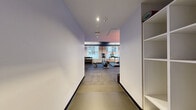 Located at 1 India St in Boston's historic waterfront neighborhood, this fitness center offers a well-appointed exercise space designed for efficient, focused workouts. The room features durable rubber tile flooring throughout, providing both safety and comfort underfoot. A striking dark textured ceiling contrasts with clean white walls, while linear LED lighting creates a modern, energetic atmosphere. Natural light filters in through street-facing windows, offering views of the surrounding Boston streetscape.

The space is thoughtfully organized to accommodate a range of workout types. Cardio equipment includes Life Fitness treadmills, an elliptical machine, and indoor cycling bikes positioned for easy use. A dedicated free weights area features a full dumbbell rack alongside a weight bench, catering to strength training needs. Wall-mounted flat-screen televisions are positioned throughout for entertainment during workouts. A large wall mirror enhances the sense of space and allows users to monitor their form. Additional amenities include a stability ball, battle ropes, and a mounted AED unit for safety. Built-in shelving near the entrance provides convenient storage. The overall ambiance is clean, functional, and contemporary, reflecting a professional fitness environment.